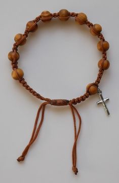 "This rosary bracelet makes a great gift or give-away for just about anyone. Each bracelet is made up of olive wood finish beads and includes a small crucifix dangle. It is strung on durable nylon cord and is completely adjustable for a variety of fits. THIS BRACELET IS TO BE USED BY MEN or WOMEN. ADJUSTS FROM 7\" - 9.5\" Material is wood and nylon cord. This listing is for (1) Bracelet BEADS: Beads have are made of wood and are round in shape. They measure approx. 1/4\" in diameter. Beads are c Adjustable Brown Hand-strung Rosary, Adjustable Crucifix Jewelry With Wooden Beads, Adjustable Brown Wooden Beads Rosary Bracelet, Adjustable Wooden Bead Crucifix Jewelry, Bracelet With Cross, Sign Of The Cross, Rosary Bracelet, Rose Scented Products, Earthy Colors