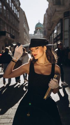 a woman in a black dress and hat walking down the street