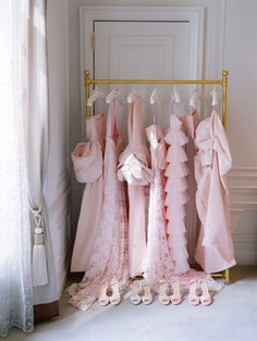 pink dresses and shoes are lined up in front of a door with white curtains on the windowsill