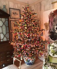 a brightly colored christmas tree in a living room next to a chair and painting on the wall