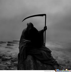 a black and white photo of a person sitting on a rock with a scythe