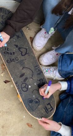 two people sitting on the ground with their feet on a skateboard that has writing on it