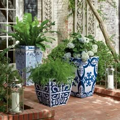 three blue and white pots with plants in them sitting on a brick walkway next to a window