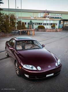 a maroon sports car is parked in front of a building with an empty parking lot