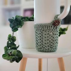 a crocheted coffee cup holder with a ladybug on it and a plant next to it