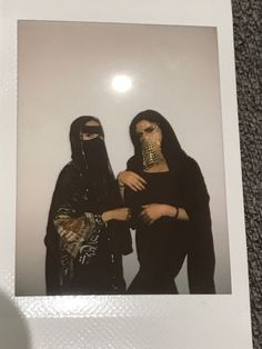 two women dressed in black standing next to each other with their faces covered by masks