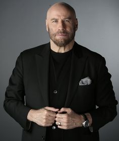 a bald man in a black suit with his hands folded