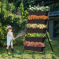 a young boy watering flowers in the garden with a hose and sprayer on his head