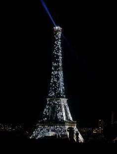 the eiffel tower is lit up at night with lights on it's sides