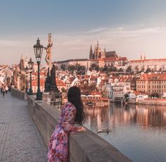 a woman is standing on a bridge looking at the water and buildings in the background