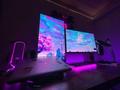 two computer monitors sitting on top of a desk in front of purple lights and other electronic equipment