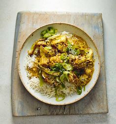 a white plate topped with rice and chicken next to a wooden board on top of a table