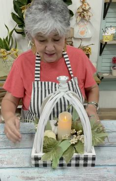 an older woman making a candle holder out of wickers and fake flowers on a table