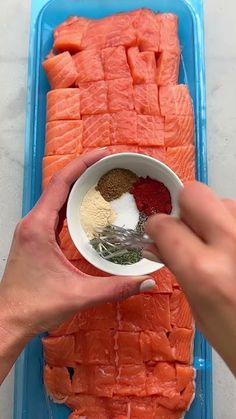 two hands holding a spoon over a bowl filled with salmon