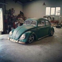 an old green vw bug in a garage next to other cars and junk cans