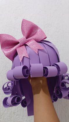 a hand holding up a purple paper doll with a pink bow on it's head