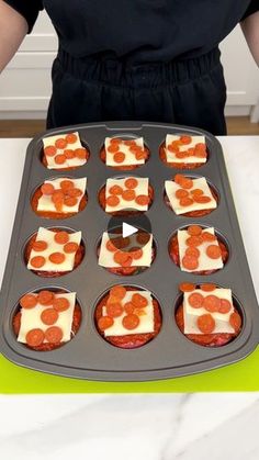 a person holding a pan filled with cupcakes on top of a green counter