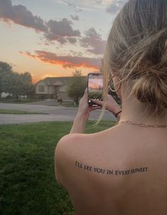 a woman with a tattoo on her back taking a selfie in front of the sunset