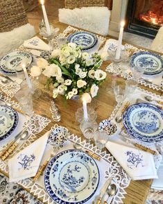 a table set with blue and white plates, silverware, candles and flowers on it