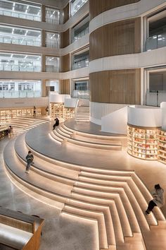 people are sitting on benches in the middle of a large room with stairs and bookshelves