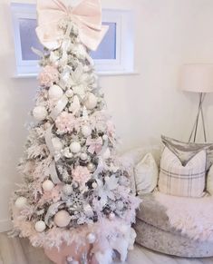 a decorated christmas tree with pink and white ornaments in a living room next to a couch