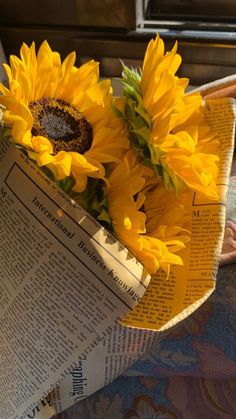 two sunflowers sitting on top of an open newspaper