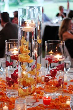 a table topped with lots of glass vases filled with water and flowers next to candles