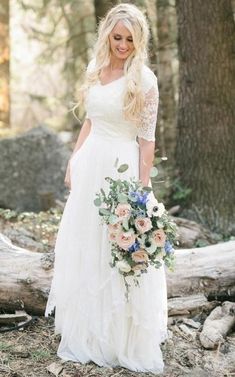 a woman in a white dress holding a bouquet and posing for the camera with trees in the background