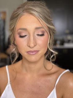 a woman with blonde hair wearing a white tank top looking down at her eye shadow