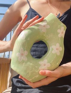 a woman is holding a green doughnut shaped like a flowered donut in her hands