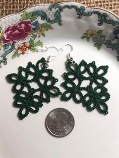 green crochet earrings on top of a white plate next to a quarter penny