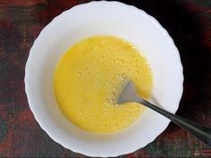 a white bowl filled with yellow liquid on top of a wooden table next to a spoon