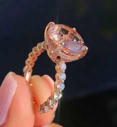 a close up of a person's hand holding a ring with an oval shaped diamond