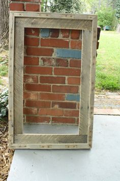 a wooden frame sitting on top of a cement slab in front of a brick wall