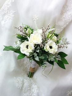 a bridal bouquet with white flowers and greenery on a lace covered bed sheet