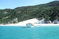 a boat in the water near a beach with white sand and green mountains behind it