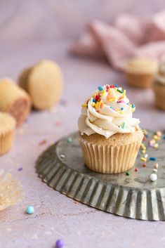 a cupcake with white frosting and sprinkles sits on a plate