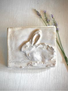 a ceramic tile with a rabbit on it and some lavenders in the back ground