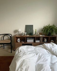 a bed with white sheets and pillows next to a wooden shelf filled with books on top of it