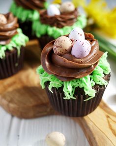 chocolate cupcakes with green frosting and mini eggs in the middle on a wooden board