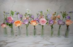 six vases filled with different types of flowers on a marble counter top in front of a marble wall