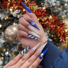 These long stiletto nails create a stunning winter wonderland look with their mix of frosty designs. A deep royal blue base complements the glittering silver snowflakes and candy cane-striped accents, while clear nails adorned with white snowflakes add a soft, ethereal touch. The bow detail on one nail brings a festive element, making this design perfect for the holiday season. Blue And White Christmas Nails, Blue Christmas Nail Designs, White Christmas Nails, White Stiletto Nails, Blue And White Christmas, Candy Cane Nails, Long Stiletto Nails, Snowflake Nails