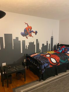 a bedroom with a spiderman mural on the wall next to a bed and desk