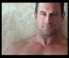 a shirtless man laying on a fluffy white carpet looking at the camera with blue eyes