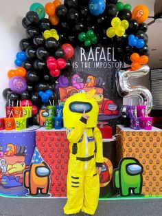 a man in a yellow space suit standing next to some colorful balloons and presents on the wall