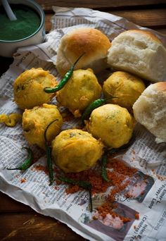 some bread rolls and green peppers on top of newspaper with dipping sauce in the background