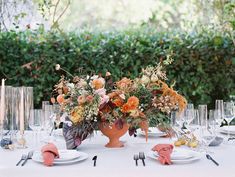 an arrangement of flowers in a vase on top of a table with plates and utensils