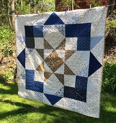 a blue and white quilt hanging on a clothes line in the grass with trees in the background