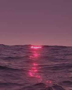 the words dream are lit up on top of the water in front of an ocean wave