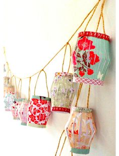 colorful paper lanterns hanging from strings on the side of a white wall with red and pink flowers